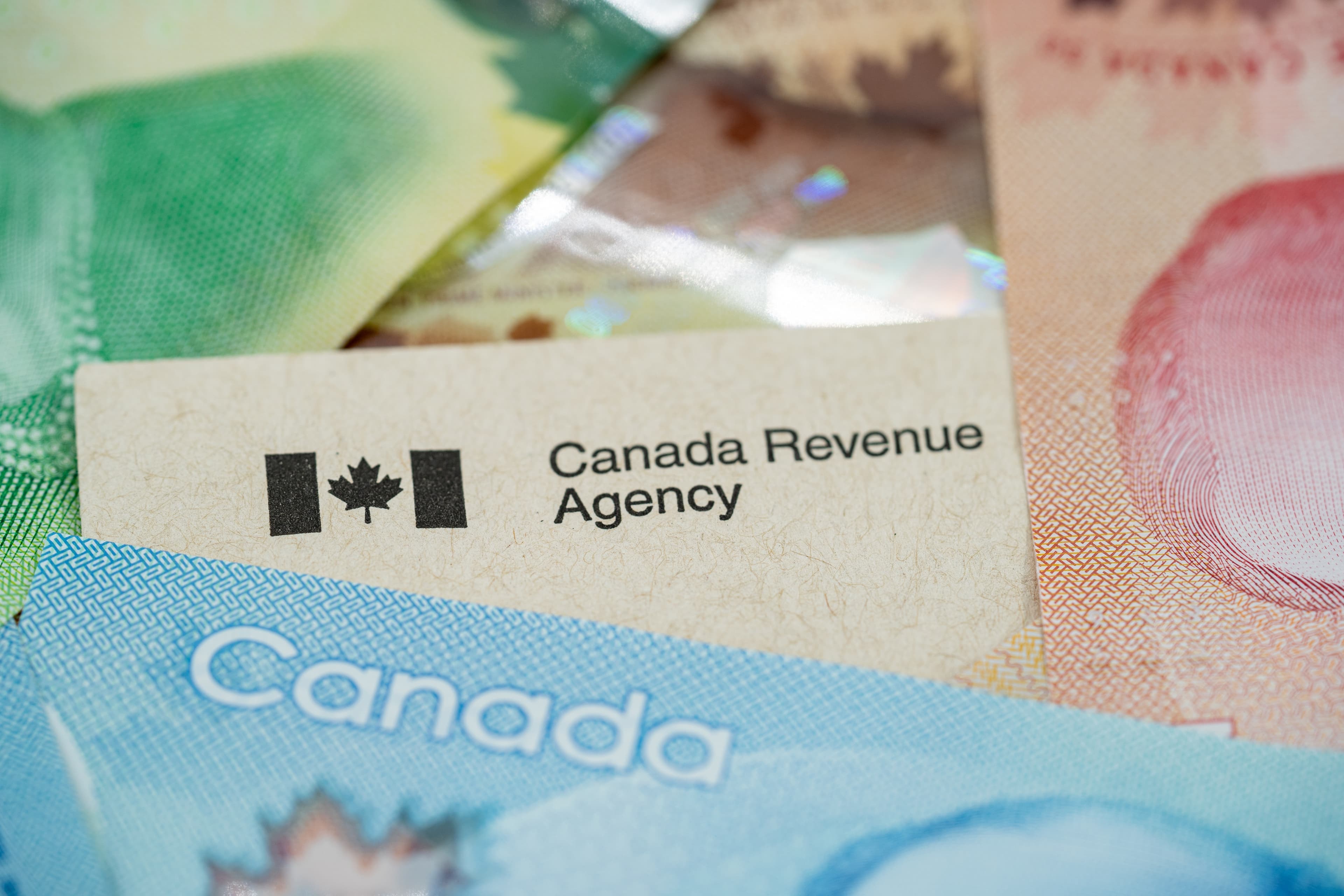 Canadian flag and "Canada Revenue Agency" text on a card, amidst various Canadian dollar bills.